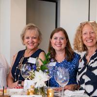 Group of four, one man and three women, standing around taller event table smiling at camera